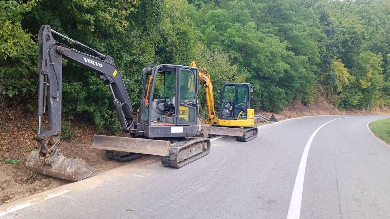 Dva mini bagera otvaraju jamu uz ivicu asfaltnog puta