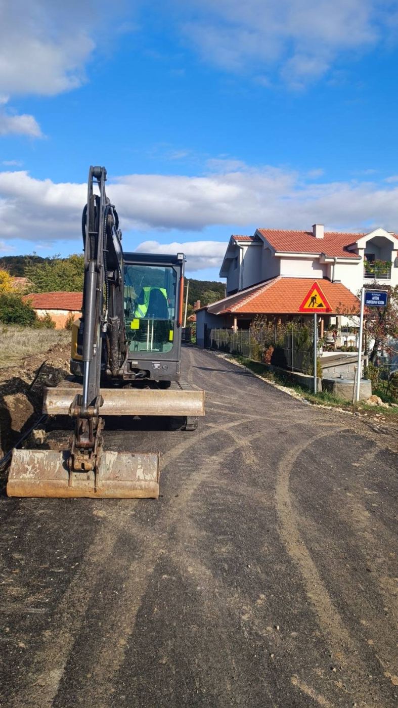 Mini bager na novom asfaltu pored iskopanog rova i znaka radovi na putu